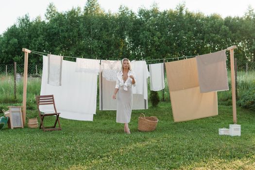 Laundry day. A woman hangs linen and towels on a tree in the courtyard of a village house. Summer cottage concept.
