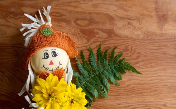 Cute stuffed toy with autumn yellow flowers. Halloween, Thanksgiving. Wooden background, space for text