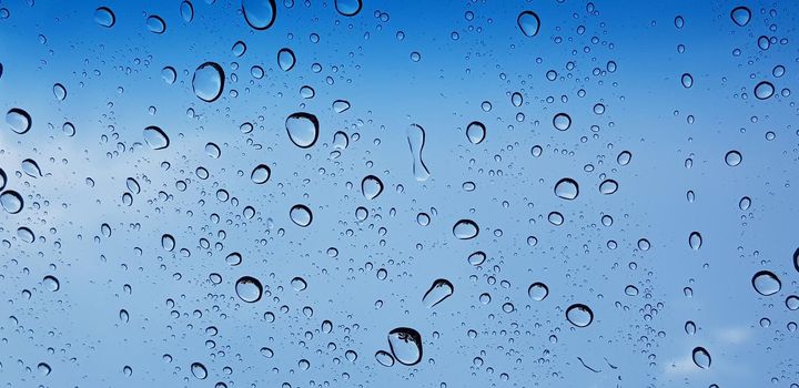 Water droplets perspective through window glass surface against blue sky good for multimedia content backgrounds