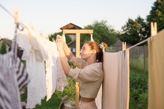 Laundry day. A woman hangs linen and towels on a tree in the courtyard of a village house. Summer cottage concept.