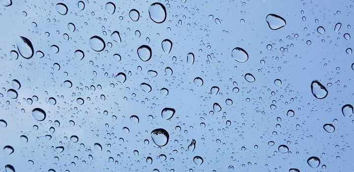 Water droplets perspective through window glass surface against blue sky good for multimedia content backgrounds