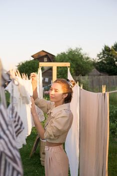 Laundry day. A woman hangs linen and towels on a tree in the courtyard of a village house. Summer cottage concept.