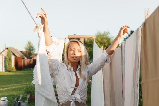 Laundry day. A woman hangs linen and towels on a tree in the courtyard of a village house. Summer cottage concept.