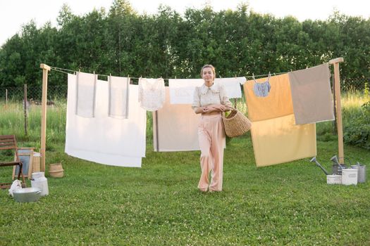 Laundry day. A woman hangs linen and towels on a tree in the courtyard of a village house. Summer cottage concept.