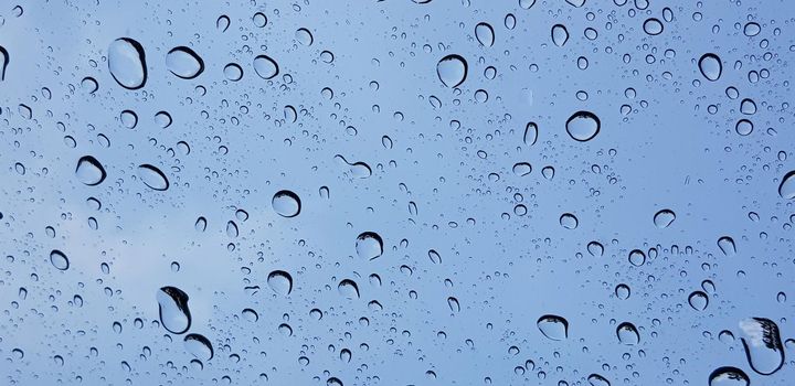 Water droplets perspective through window glass surface against blue sky good for multimedia content backgrounds