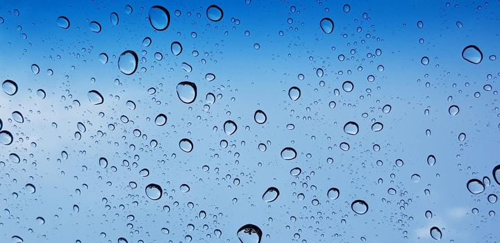 Water droplets perspective through window glass surface against blue sky good for multimedia content backgrounds