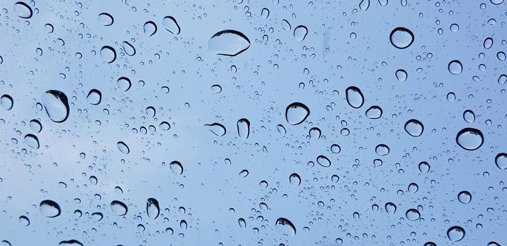 Water droplets perspective through window glass surface against blue sky good for multimedia content backgrounds