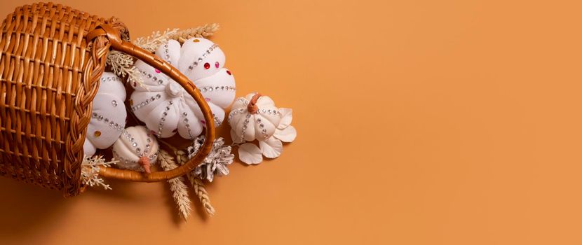 Banner with white decorative pumpkins with shiny stones and pine cones in basket on colored background with copy space.