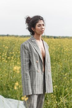 An Asian model poses in a field of yellow flowers for a clothing brand, polyethylene is the main props for a photo shoot. The concept of manufacturing clothing from recycled plastic. A woman in a pantsuit is standing on a plastic bag.