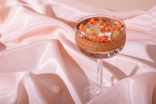 Still life from glass and water with mountain ash and dried leaf on folded fabric background. Minimalistic creative autumn concept.