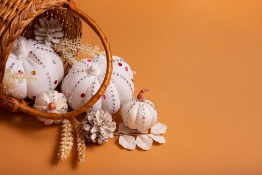 White decorative hand made pumpkins with shiny stones and pine cones in basket on colored background. Autumn harvest concept.