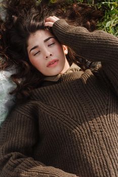 An Asian woman is lying on the ground in a field in a brown sweater. The concept of manufacturing clothing from recycled plastic. An Asian woman is lying on a plastic bag. Portrait of a dark-haired woman with loose hair.