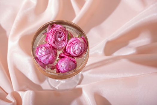 Top view bulbs in champagne around roses in the glass on folded textile background. Creative beautiful still life.