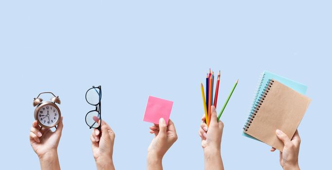 School stationary in female hands on blue background. Notebook, pencils and other tools with alarm clock isolated on blue. Banner back to school concept.