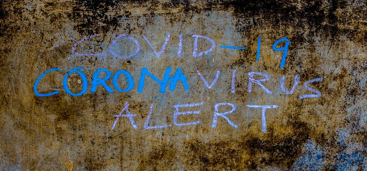 Creative shot of Covid 19 or Coronavirus alert written on a rough wall with chalk, horizontal shot.