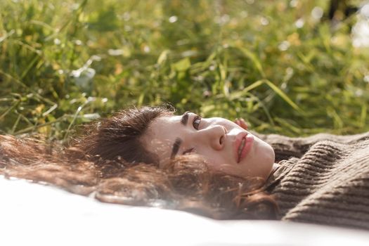 An Asian woman is lying on the ground in a field in a brown sweater. The concept of manufacturing clothing from recycled plastic. An Asian woman is lying on a plastic bag. Portrait of a dark-haired woman with loose hair.