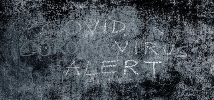 Creative shot of Covid 19 or Coronavirus alert written on a rough wall with chalk, horizontal shot.