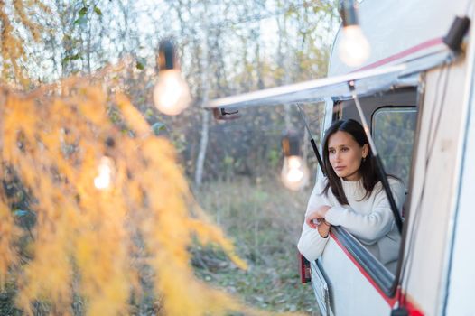 Portrait of a caucasian woman looking out of a trailer window. Travel in a camper in autumn