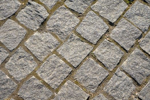 Chipped stone pavement background texture, cobbled street in sunlight.