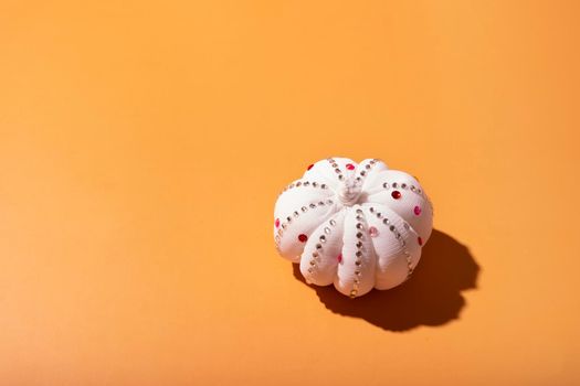 White decorative textile pumpkin with shiny stones with copy space. Autumn minimal harvest concept. Orange background.