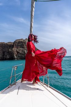Attractive middle-aged woman in a red dress on a yacht on a summer day. Luxury summer adventure, outdoor activities