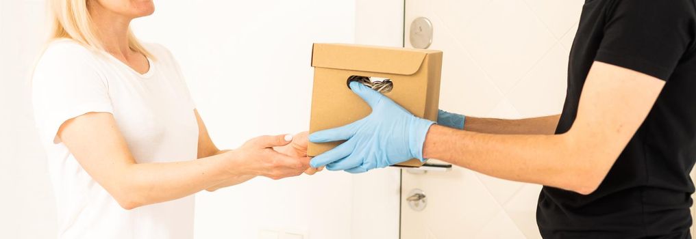 Courier in protective mask and medical gloves delivers takeaway food. Delivery service under quarantine, disease outbreak, coronavirus covid-19 pandemic conditions