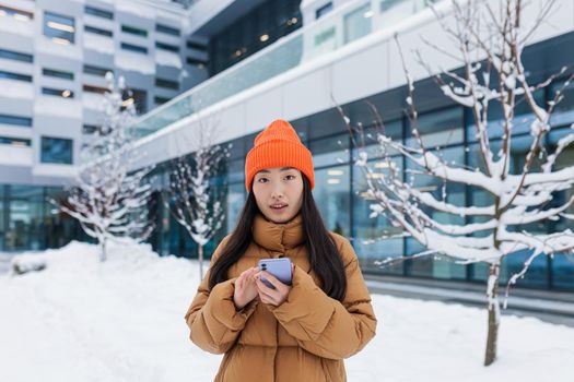 Beautiful Asian girl uses the phone, online dating, makes a choice, walks on a winter snowy day