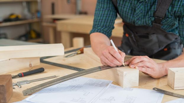 A carpenter measures wooden planks and makes marks with a pencil in a workshop