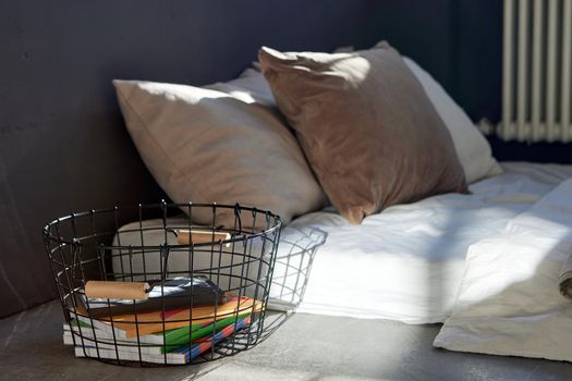 Soft mattress with pillows and blanket placed on floor near metal basket with various colorful books in bedroom