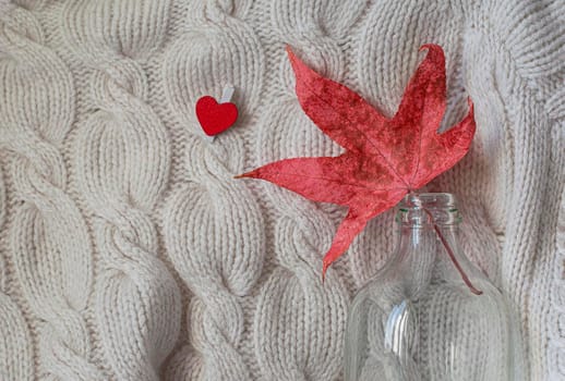 Hello autumn. Creative flat lay composition on light background. Red leaf, knitted sweater and small heart. Copy space.