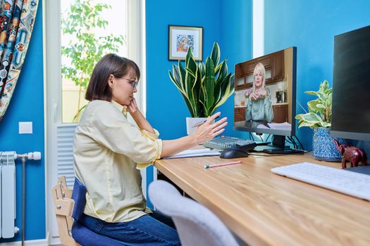 Middle aged woman talking online with mature female video call on computer, home interior. Virtual meeting, therapy session with psychologist. Chat conference technology psychology education business