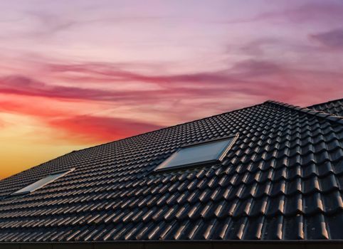 Open roof window in velux style with black roof tiles during sunset
