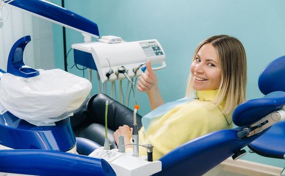 Beautiful girl patient shows the class with her hand while sitting in the Dentist's chair.