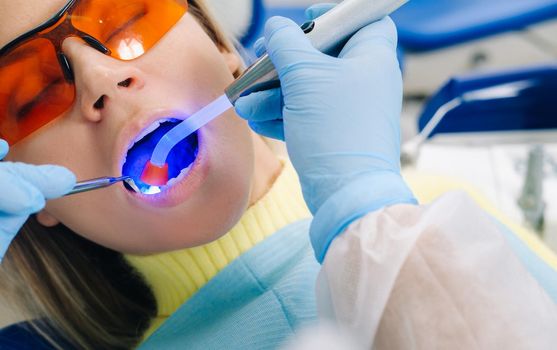 A young beautiful girl in dental glasses treats her teeth at the dentist with ultraviolet light. filling of teeth.