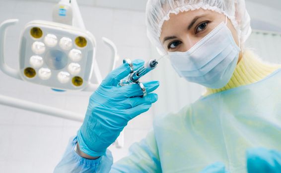 A masked dentist holds an injection syringe for a patient in the office.