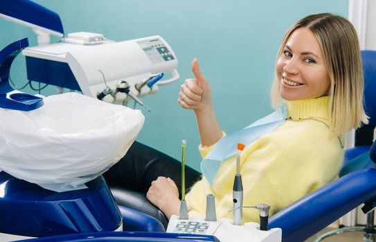 Beautiful girl patient shows the class with her hand while sitting in the Dentist's chair.