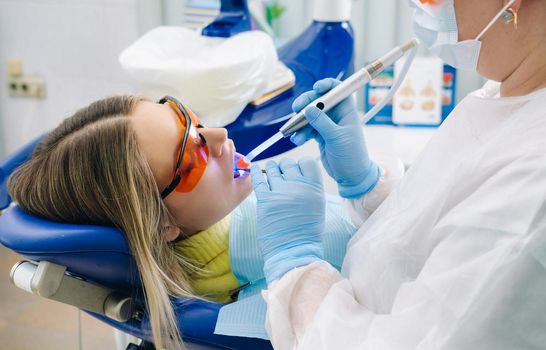 A young beautiful girl in dental glasses treats her teeth at the dentist with ultraviolet light. filling of teeth.