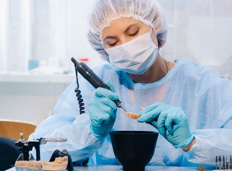 A dental technician in protective clothing is working on a prosthetic tooth in his laboratory.