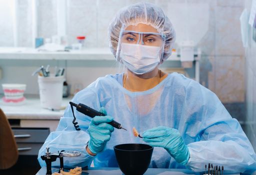 A dental technician in protective clothing is working on a prosthetic tooth in his laboratory.