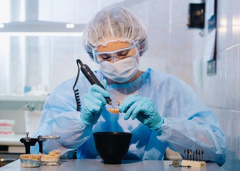 A dental technician in protective clothing is working on a prosthetic tooth in his laboratory.