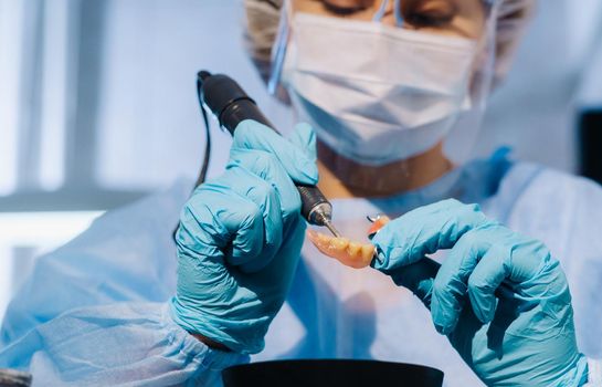 A dental technician in protective clothing is working on a prosthetic tooth in his laboratory.