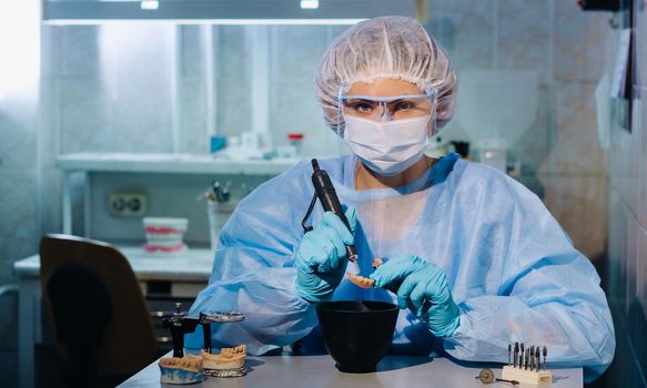 A dental technician in protective clothing is working on a prosthetic tooth in his laboratory.