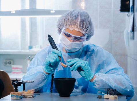 A dental technician in protective clothing is working on a prosthetic tooth in his laboratory.