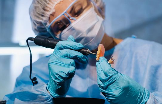 A dental technician in protective clothing is working on a prosthetic tooth in his laboratory.