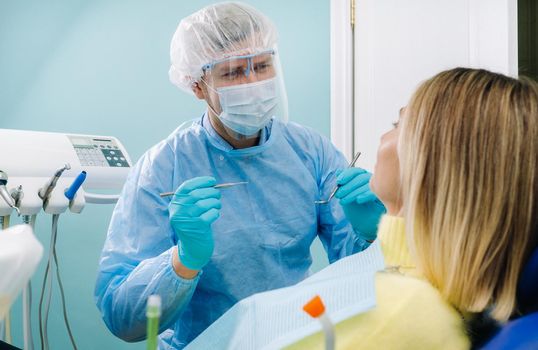 The patient smiles in the dentist's chair in a protective mask and instrument before treatment in the dental office.