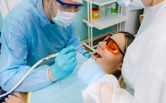 A male dentist with dental tools drills the teeth of a patient with an assistant. The concept of medicine, dentistry and healthcare.