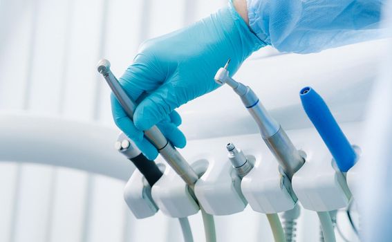 a dentist wearing gloves in the dental office holds a tool before working.