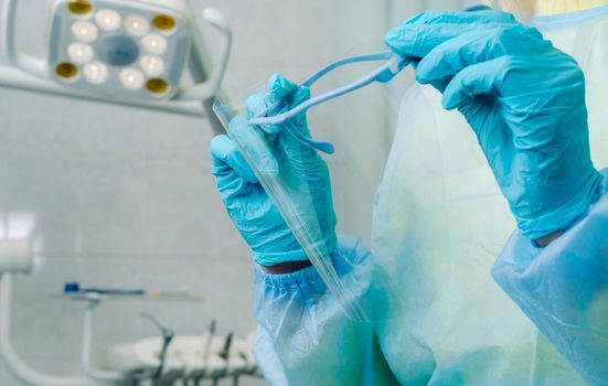 close up of a dentist's hands holding a protective plastic screen in his office.