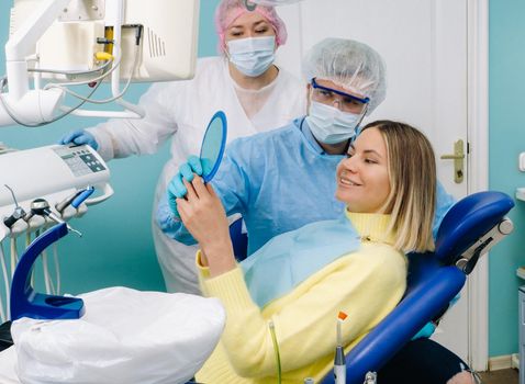 The dentist shows the client the results of his work in the mirror.The client smiles.