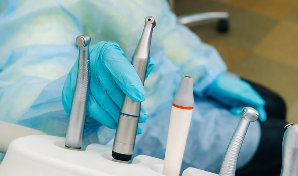 a dentist wearing gloves in the dental office holds a tool before working.